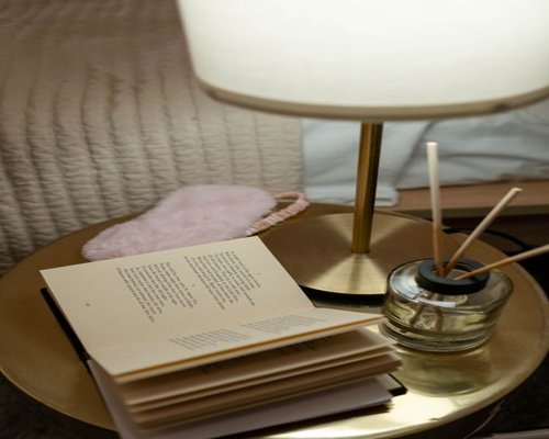 An open book lying on a nightstand under a warm focused light from a bedside reading lamp
